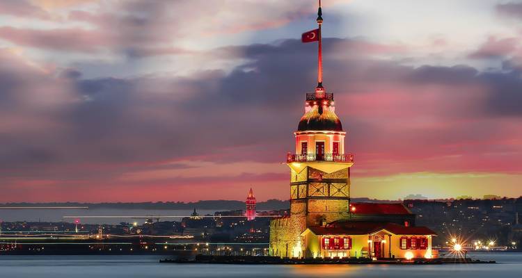 Illuminated tower at sunset with city skyline in the background.