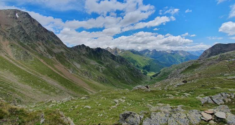 Vue panoramique d'une vallée de montagne avec un ciel bleu clair et des nuages épars.