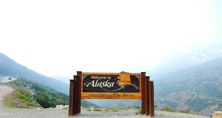 Welcome to Alaska sign with a mountain backdrop.