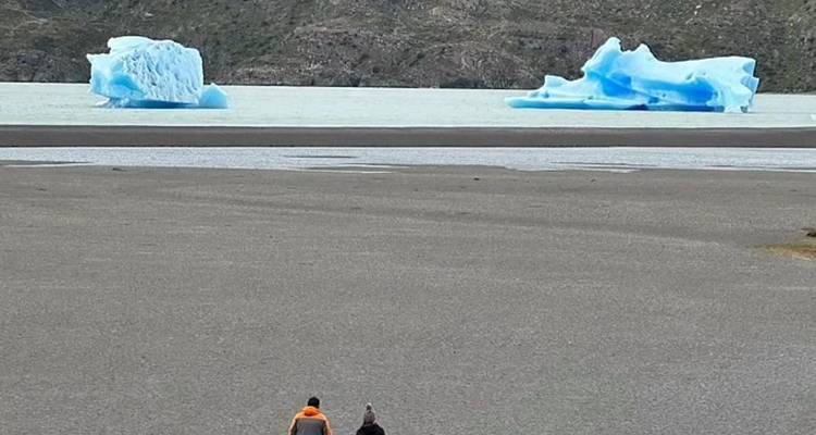 Twee mensen die naar ijsbergen lopen op een strand met heuvels in de verte.