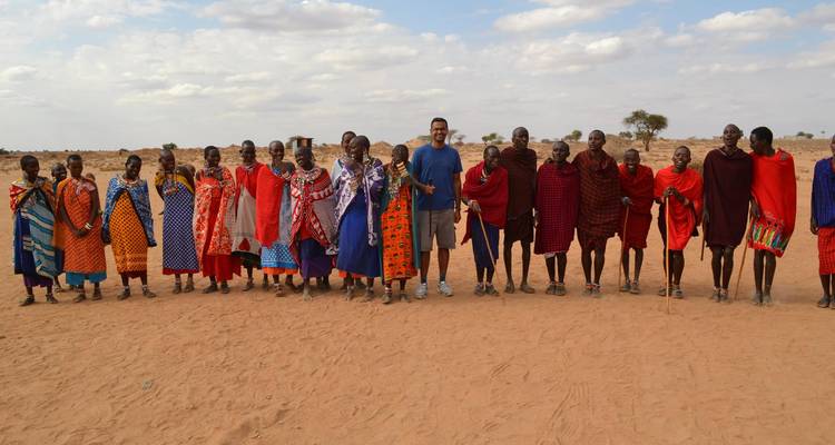 Gruppe von Menschen in traditioneller Kleidung in einer Reihe auf sandigem Boden.