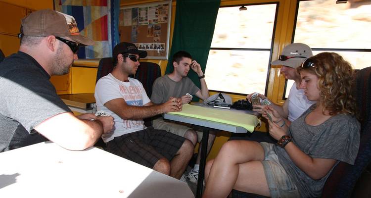Young travelers sitting around a table inside an overland truck playing cards during transit.