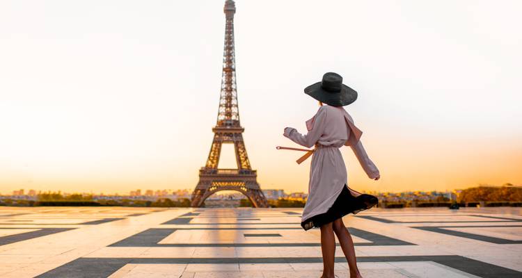 Person in a hat near the Eiffel Tower at sunset.