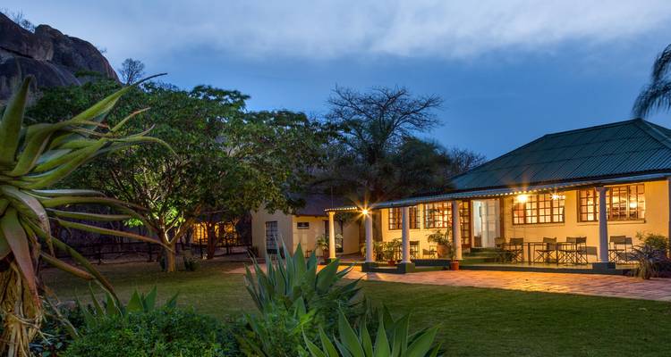 Kolonialer Lodge mit Garten, abends beleuchtet.