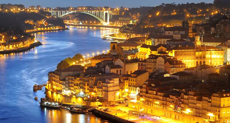 Scenic night view of Porto with city lights illuminating buildings and a bridge over a river.