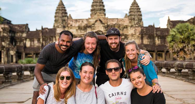 Un grupo sonriente de jóvenes viajeros posa junto frente a las torres de piedra de Angkor Wat.