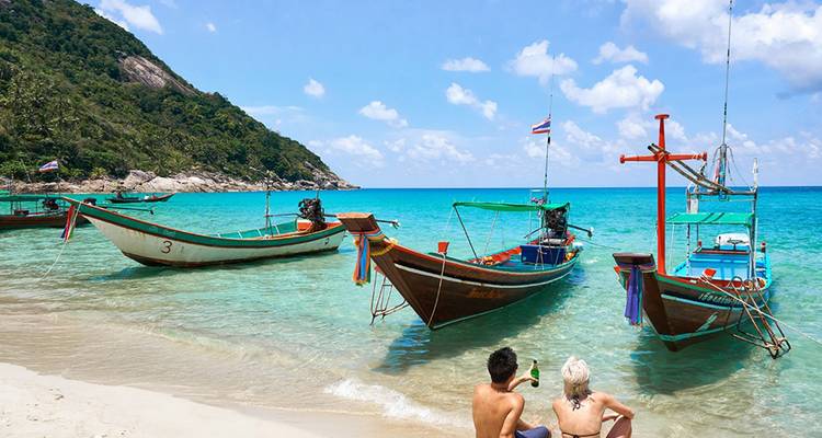 Two people relaxing on a beach near colorful boats.