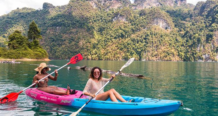 Twee vrienden peddelen in felgekleurde kajaks over een turquoise meer omringd door met jungle bedekte kalkstenen kliffen.