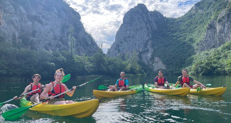 Cinq kayakistes en kayaks sit-on-top jaunes pagaient sur une eau verte et calme sous les parois escarpées d'un canyon calcaire, sous un ciel partiellement nuageux.
