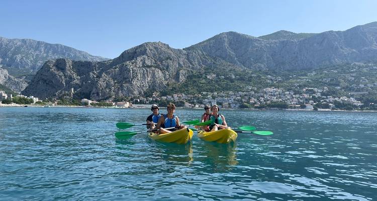 Deux kayaks en tandem avec des voyageurs pagaient au large, face aux montagnes côtières accidentées et à la ville d'Omiš.