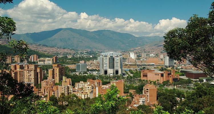 Vue panoramique de la skyline moderne de Medellín encadrée par des collines verdoyantes et des montagnes couronnées de nuages.
