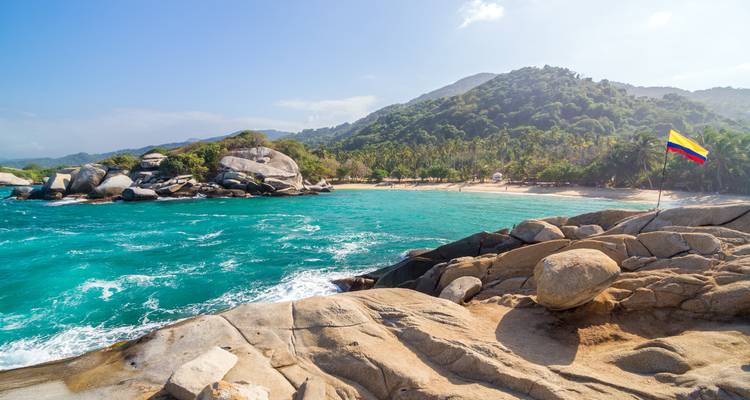 Plage immaculée avec côte rocheuse et drapeau colombien.