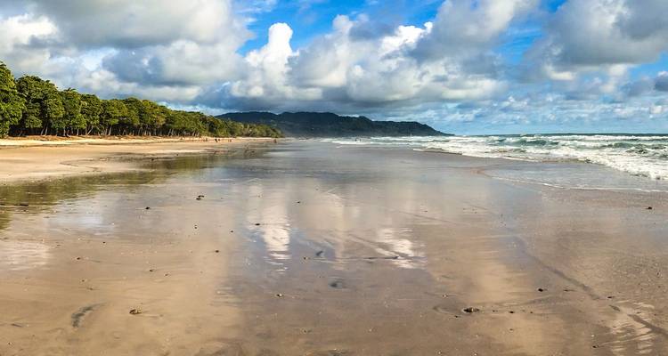 Playa de arena blanca en la costa del Pacífico de Costa Rica con olas suaves y una punta rocosa cubierta de exuberante vegetación