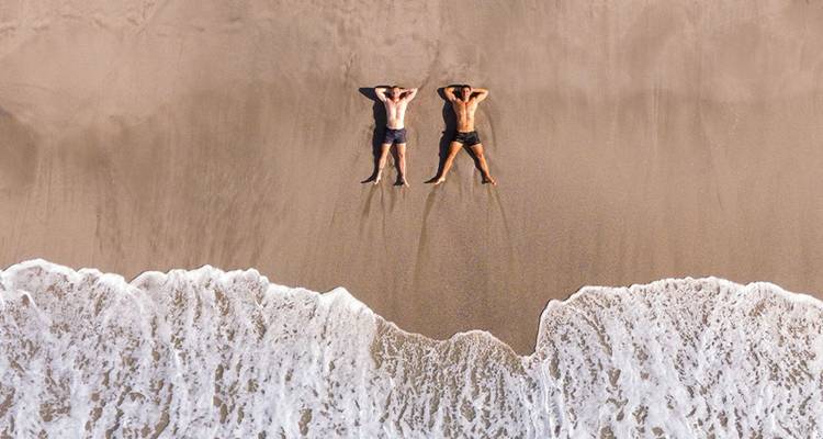 Toma aérea de dos personas acostadas en la arena mojada en la orilla de las olas que se acercan del océano