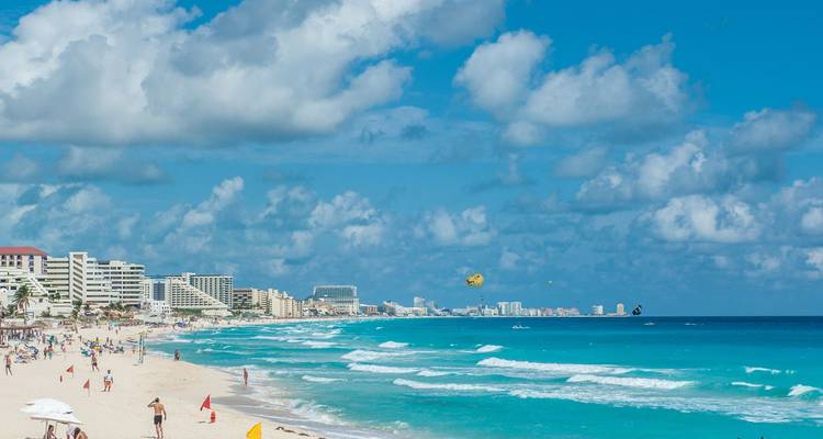 Breed wit zandstrand omzoomd door resorts en turquoise water met parasailing vliegers aan de hemel.