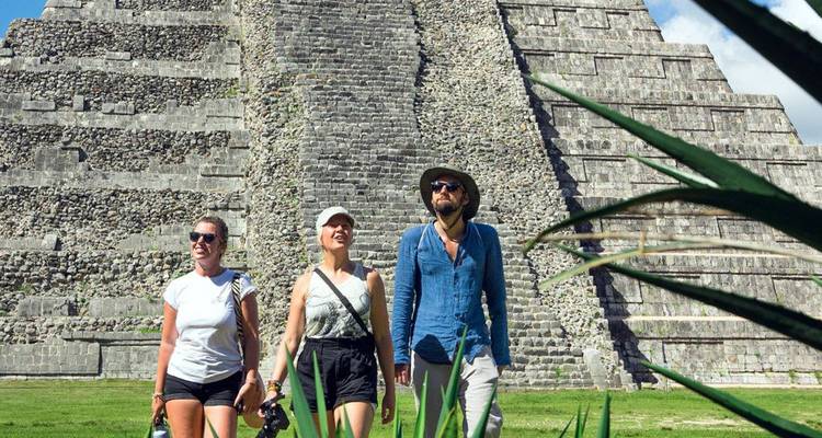 Drie toeristen die op een zonnige dag naast de stenen piramide van Chichen Itza lopen.