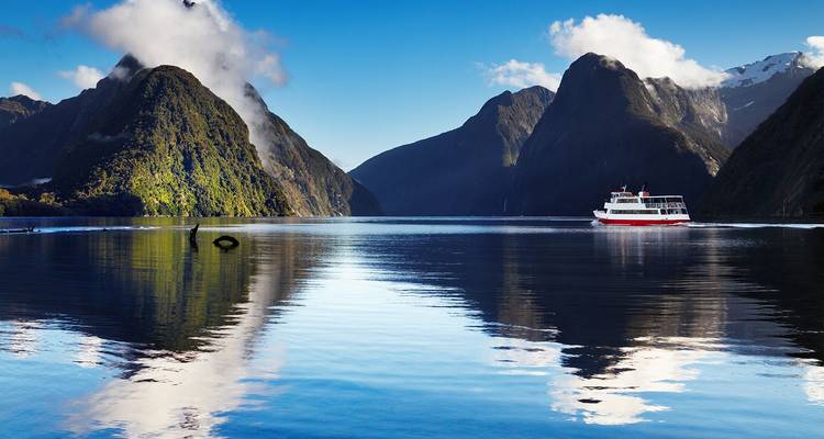 Kreuzfahrtschiff, das über den spiegelglatten Milford Sound gleitet, mit majestätischen nebligen Gipfeln, die sich perfekt widerspiegeln