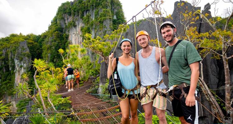 Drie avontuurlijke reizigers met harnas om poseren op een zwevende loopbrug hoog boven een kalksteenkasteel jungle.