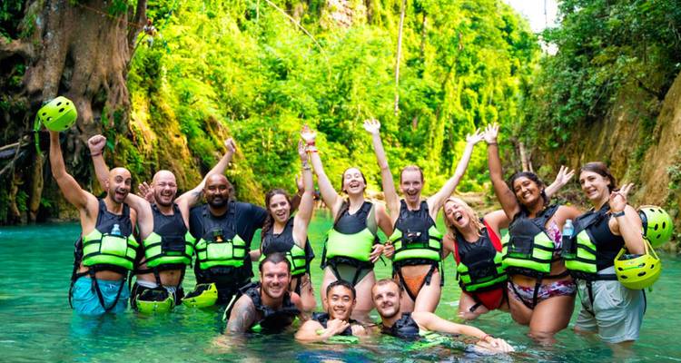 Groupe heureux portant des gilets de sauvetage néon célébrant dans une eau cristalline entourée de parois de canyon luxuriantes.