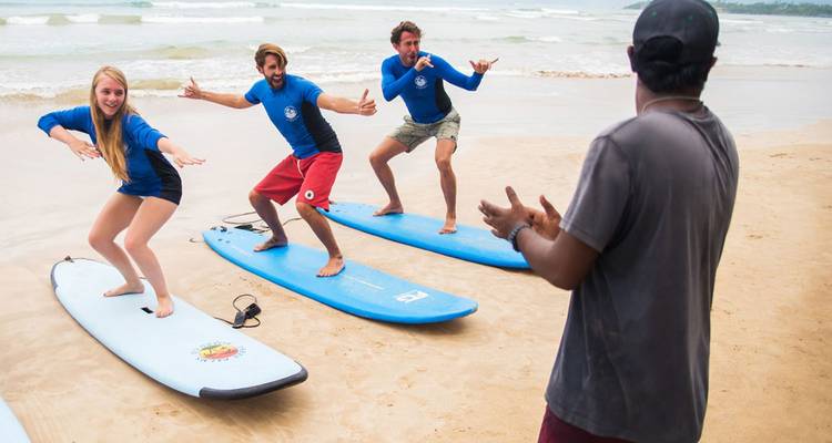 Moniteur de surf coaching trois jeunes voyageurs s'exerçant à la stance sur des planches le long d'une plage sablonneuse du Sri Lanka