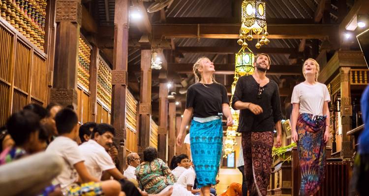 Les voyageurs vêtus de sarongs colorés marchent dans un hall en bois orné lors d'une cérémonie culturelle au Sri Lanka