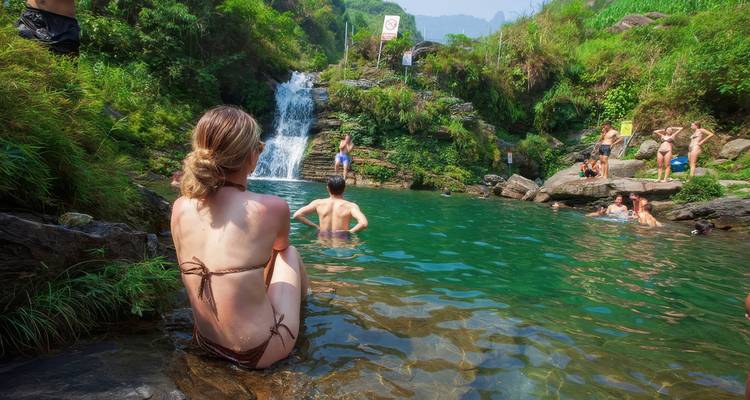 Personas nadando en una piscina natural en un entorno exuberante y verde con una cascada.