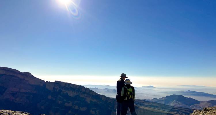 Zwei Wanderer im Silhouetten gegen ein riesiges Bergtal unter intensivem Sonnenlicht