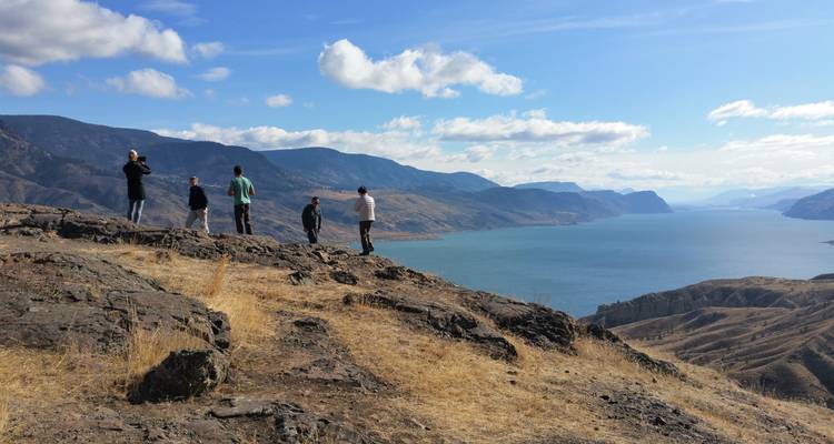 Menschen stehen auf felsigem Gelände und blicken auf einen großen See.