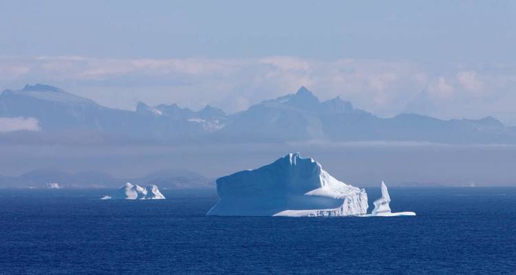 Icebergs floating in vast ocean with mountainous backdrop.