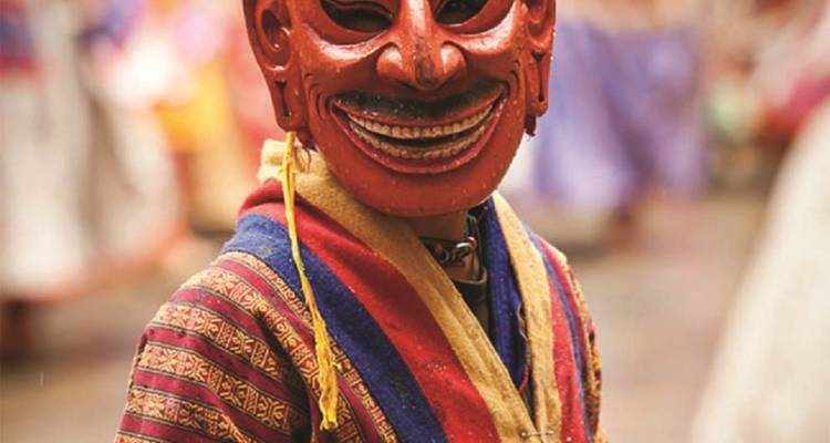 Un artiste bhoutanais porte un masque rouge vif et un costume traditionnel lors d'un festival culturel.