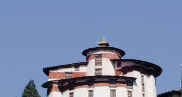 Gros plan des étages supérieurs d'une tour de forteresse bhoutanaise blanche contre un ciel bleu clair.