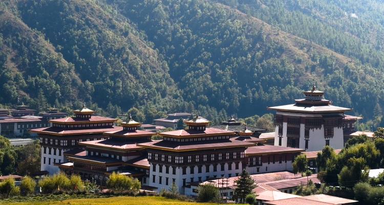 Un vaste complexe monastique dzong s'étend sur le fond d'une vallée encadrée par des sommets boisés.