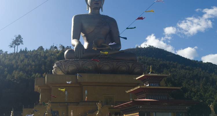 La massive statue en bronze du Bouddha Dordenma se dresse au-dessus d'une plateforme de temple contre un ciel bleu.