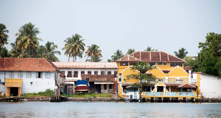 Scène au bord de l'eau avec des bâtiments colorés et des palmiers.