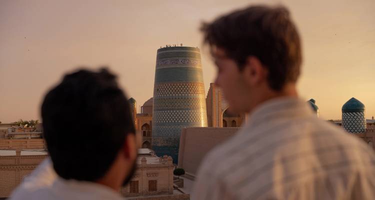 Deux voyageurs admirent le minaret Kalta Minor aux carreaux turquoise au coucher du soleil à Khiva.