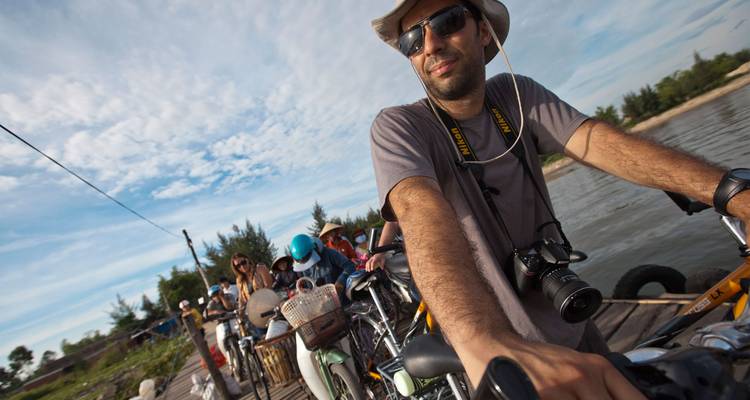 Los viajeros con bicicletas y cámaras se amontonan en un pequeño ferry mientras cruza un río tranquilo.