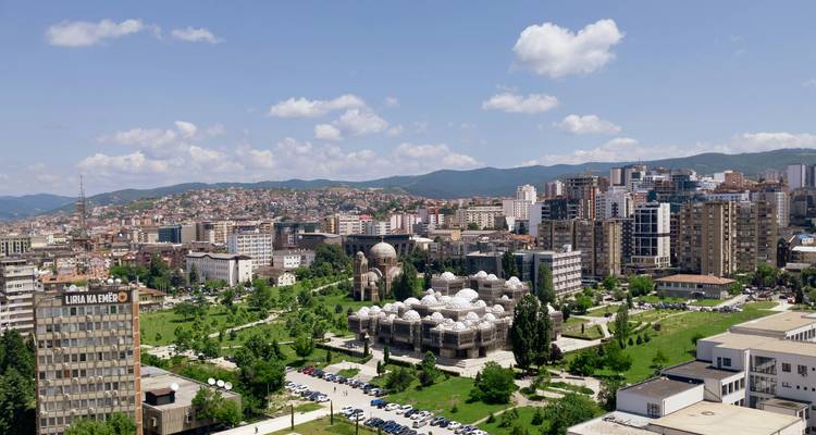 Stadtbild von Pristina mit modernen Gebäuden und einem grünen Park.