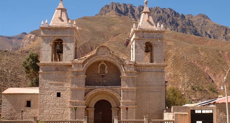 Iglesia colonial de piedra con torres gemelas ubicada contra las montañas andinas escarpadas en un pueblo de las tierras altas.