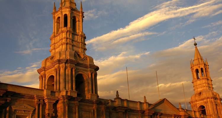 Las elegantes torres de piedra de la Catedral de Arequipa brillando con la cálida luz del atardecer contra nubes tenues.