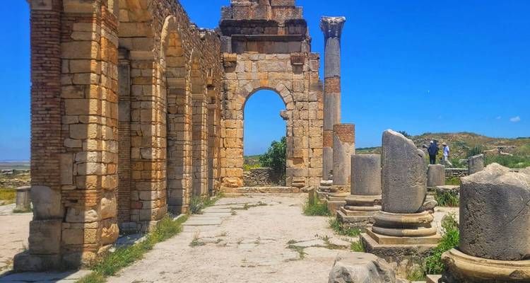 Antiker römischer Steinbogen und Säulen der Volubilis-Ruinen unter einem leuchtend blauen Himmel.