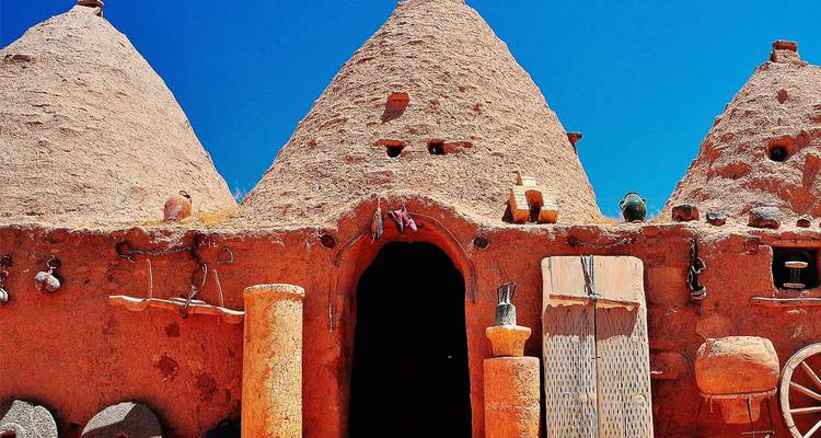 Fila de casas tradicionales en forma de colmena construidas con ladrillos de barro rojizo, decoradas con cerámica y herramientas bajo un cielo azul intenso.