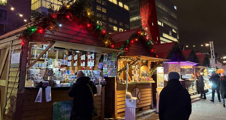 Houten kraampjes met kleurige verlichting staan opgesteld op een sneeuwbedekte kerstmarkt in Montreal 's nachts.