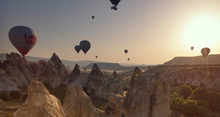 Amplia escena de docenas de globos flotando sobre el paisaje de chimeneas de hadas dentadas de Capadocia bajo la suave luz del amanecer.