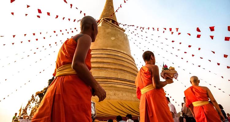 Des moines se promenant autour d'un temple doré avec des drapeaux au-dessus.