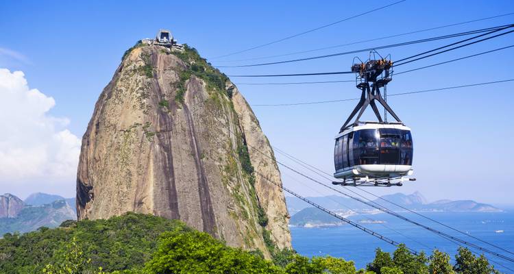 Cable car approaching a large rock mountain by the sea.
