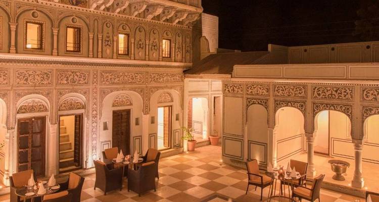 Nighttime courtyard of a heritage haveli restaurant softly lit with tables set for dinner.