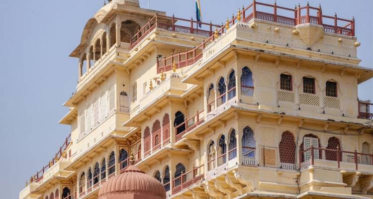 Elegant yellow sandstone palace with red railings and arched windows against clear sky.