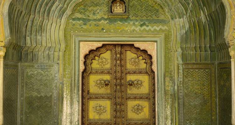 Ornate green gateway with intricate floral carvings and gilded doors inside a palace courtyard.