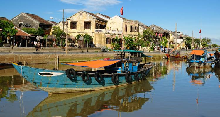 Des bateaux de pêche en bois colorés sont amarrés sur la rivière calme qui reflète les maisons-boutiques jaunes du patrimoine de Hoi An par une belle matinée ensoleillée.