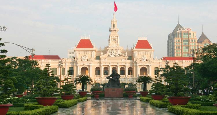 L'Hôtel de Ville de Ho Chi Minh-Ville donne sur un parc aménagé à la lumière douce du matin avec des tours de bureaux modernes en arrière-plan.